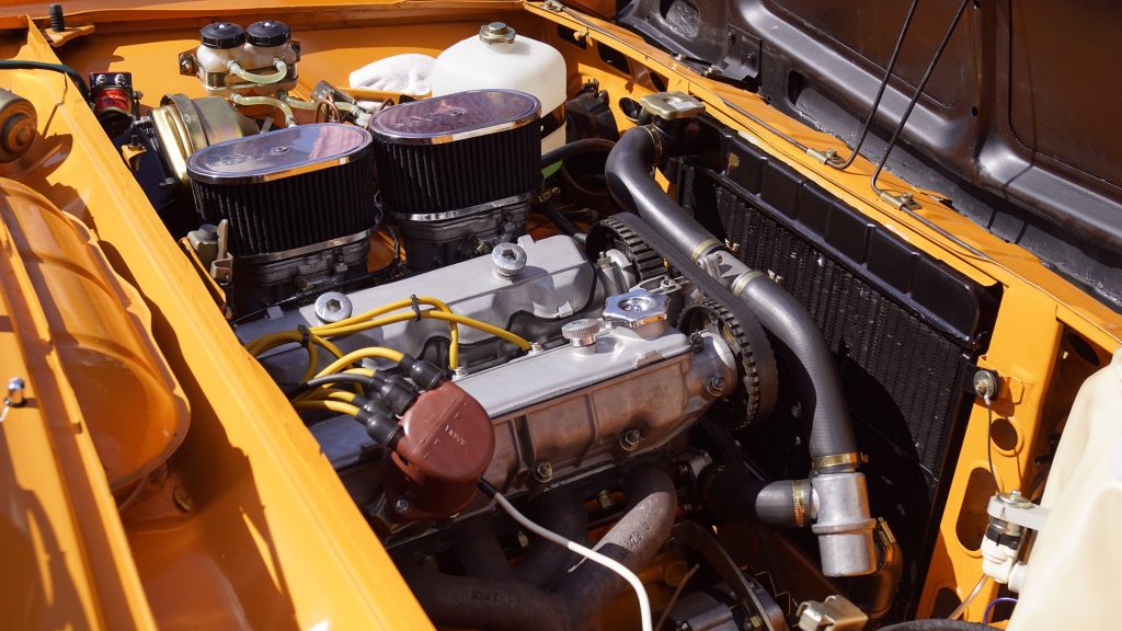 The hood of an old car is propped open, exposing the engine and its various parts.
