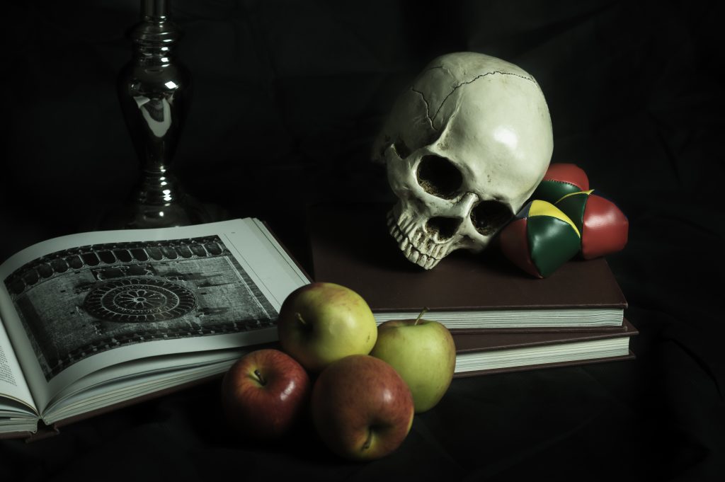 Still-life of a skull, books, a candle holder, and apples.