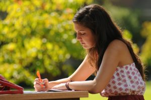 Young university student studying outside on campus. Highlighting important notes.
