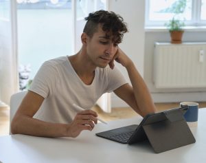 Student studying on a tablet. He has his head resting on his left hand and holding and stylus pen in the other.