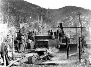 A black and white photo of a group of peoples working with equipment to render eulachon grease.