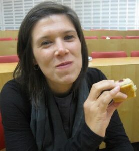 This is an image of Jennifer Brady. She is pictured mid-laughter in a classroom setting, holding a sandwich with ease. Her approachable and candid presence reflects her commitment to food justice, critical inquiry, and humanizing nutrition education.
