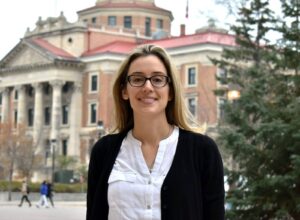 This is an image of Dr. Natalie Riediger, who stands outdoors University of Manitoba's campus. Her presence reflects a dedication to advancing health equity through collaborative and community-engaged research.
