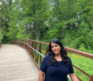 An image of Safeena Jabar standing on a wooden bridge with trees in the background. In 2022, while she was a Master’s student at TMU, she created the original Anti-Black Racism in Dietetics PowerPoint presentation that inspired the development of this Pressbook.
