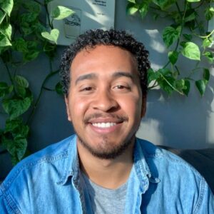 An image of Sheldomar Elliott, a Black urban farmer and food justice advocate seated in a plant-filled setting. Sheldomar’s calm energy reflects his deep connection to land, culture, and youth empowerment.