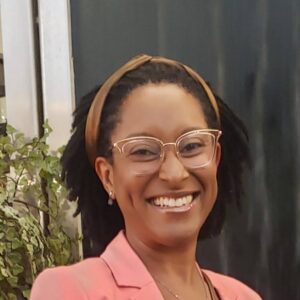 An image of Zoe Barnett, a Registered Dietitian with a warm smile standing with plants. Her joy and commitment to inclusive, community-based nutrition are evident in her presence.