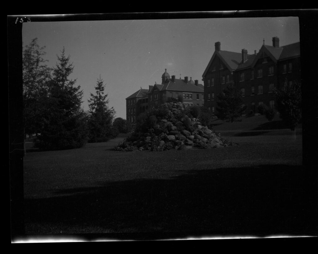 Black and white photograph of the Orillia Asylum for the Insane, taken in August 1909. The large institutional building features a central clock tower, multiple chimneys, and a sprawling lawn in front. The structure is symmetrical, with several wings extending outward, exemplifying early 20th-century asylum architecture in Ontario.