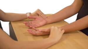 A nurse with their fingerpads placed along the radial bone of both wrists of a client taking radial pulse.