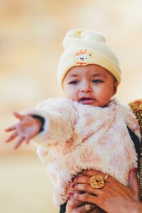 A baby stretches her arm outwards, reaching for something out of frame.