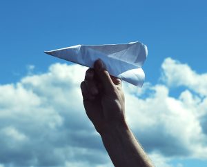 hand holding paper airplane with sky in the background.