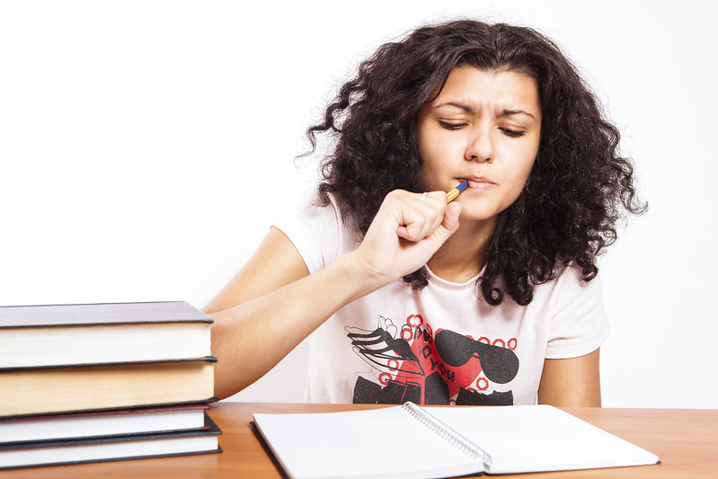 Books on the left on a desk. Student holding a pen thinking hard about the material she is reading.