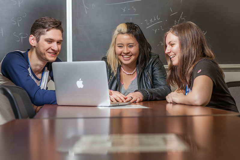 Students looking at one laptop and smiling